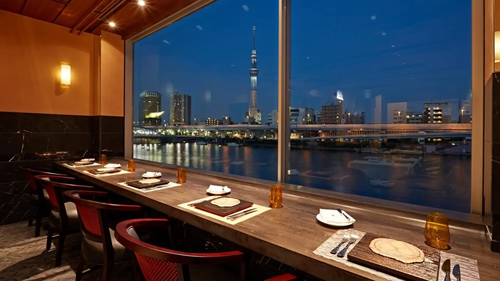 View eating area at night time with red chairs, view to water and Tokyo at Yakitori Omino.