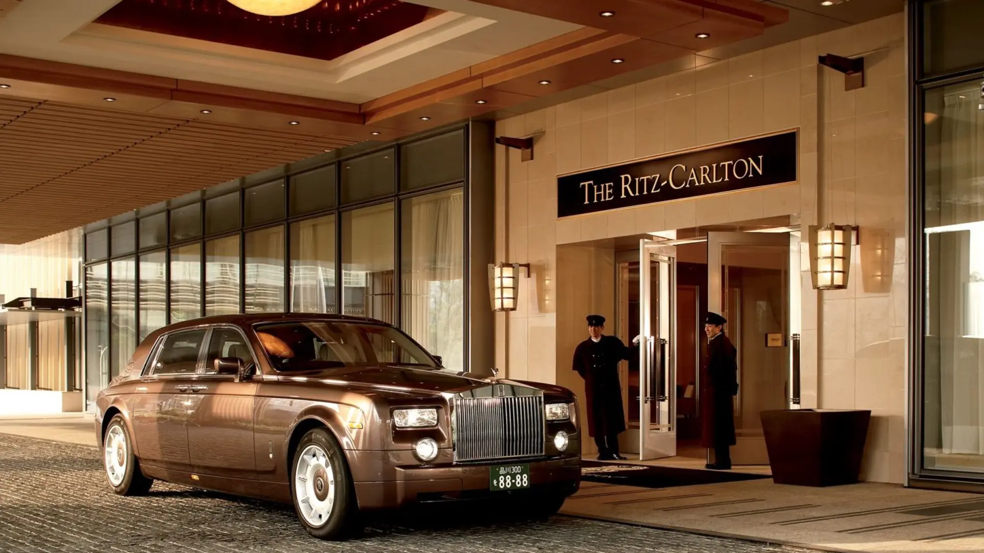 Chocolatte coloured bentley parked outside The Ritz-Carlton hotel with two men in black wellcoming guests.